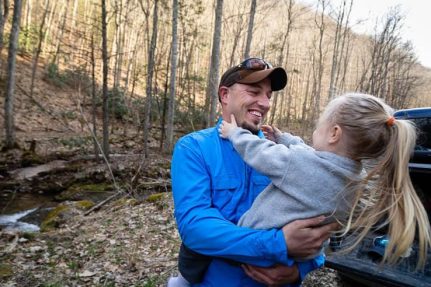 Dustin Wichterman holds his daughter as they stand by a trout stream.