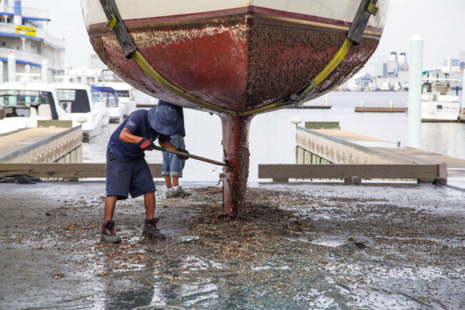 Man cleans the bottom of a boat while on pavement.