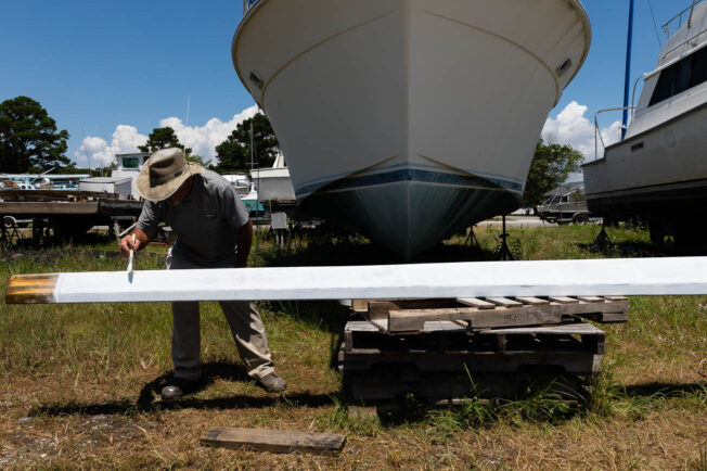 Man paints his boat on the land.