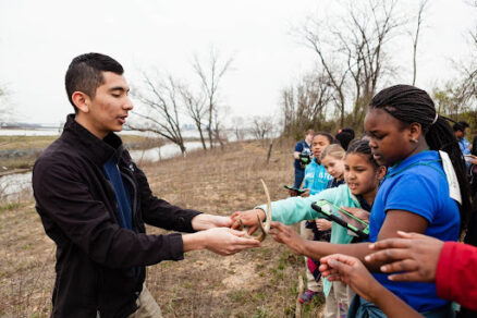 A man shoes a group of young students a deer antler on an outdoor field trip.
