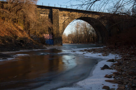 Gwynns Falls flowing through a forest and a viaduct in winter.