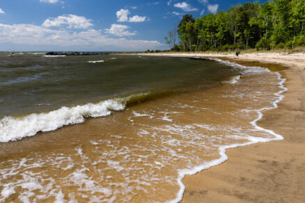Waves lap onto the shoreline at the state park with trees in the distance.