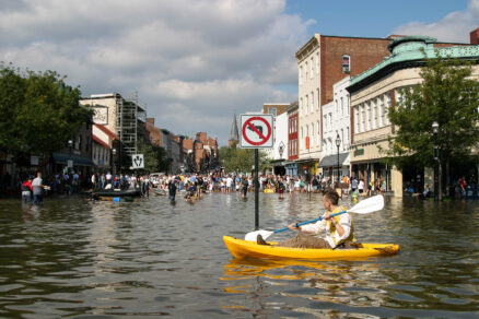 Residents walk and kayak through a flooded street.