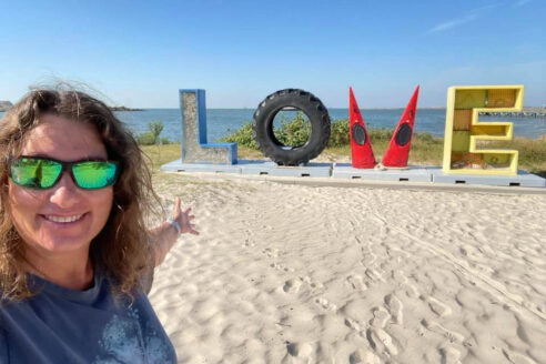 Jody, a white woman with brown hair, stands in front of a beach.