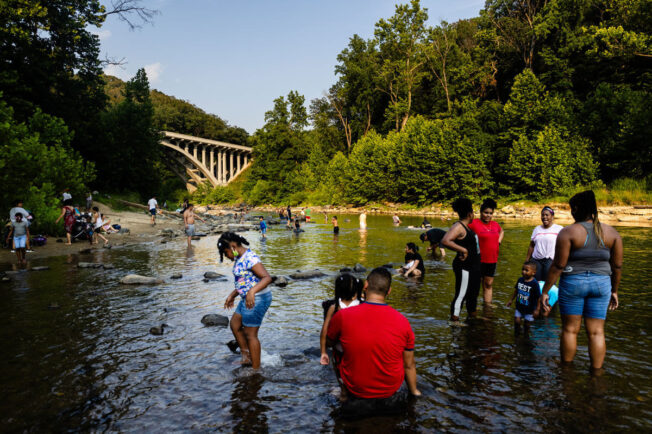 People of all ages wade and swim in the shallows of the Patapsco River.