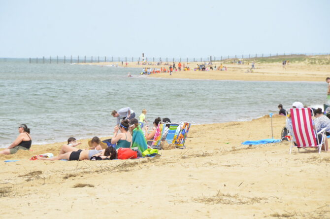 People sit on beach chairs and towels facing the water.