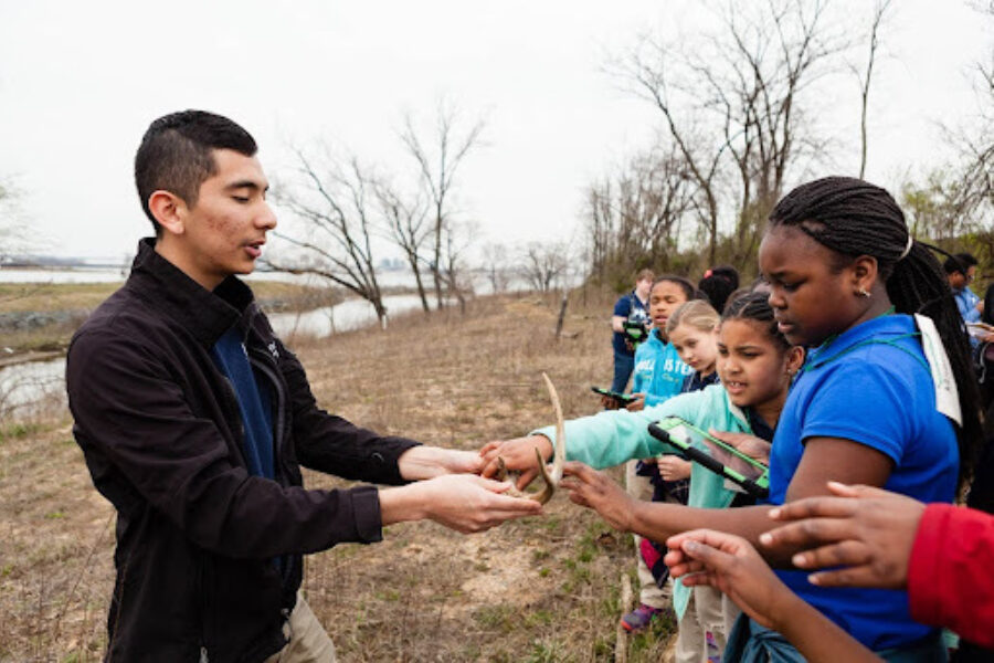 A man shoes a group of young students a deer antler on an outdoor field trip.