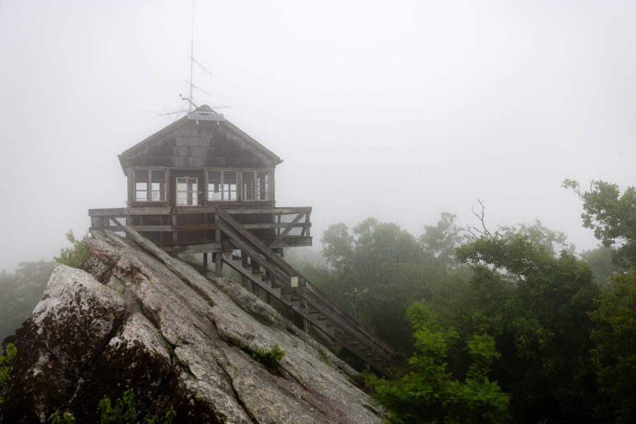 Small wooden building at the top of a rocky peek, surrounded in fog.