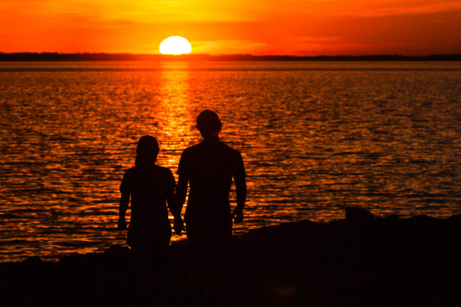Silhouette of two people watching the sunset on the water.