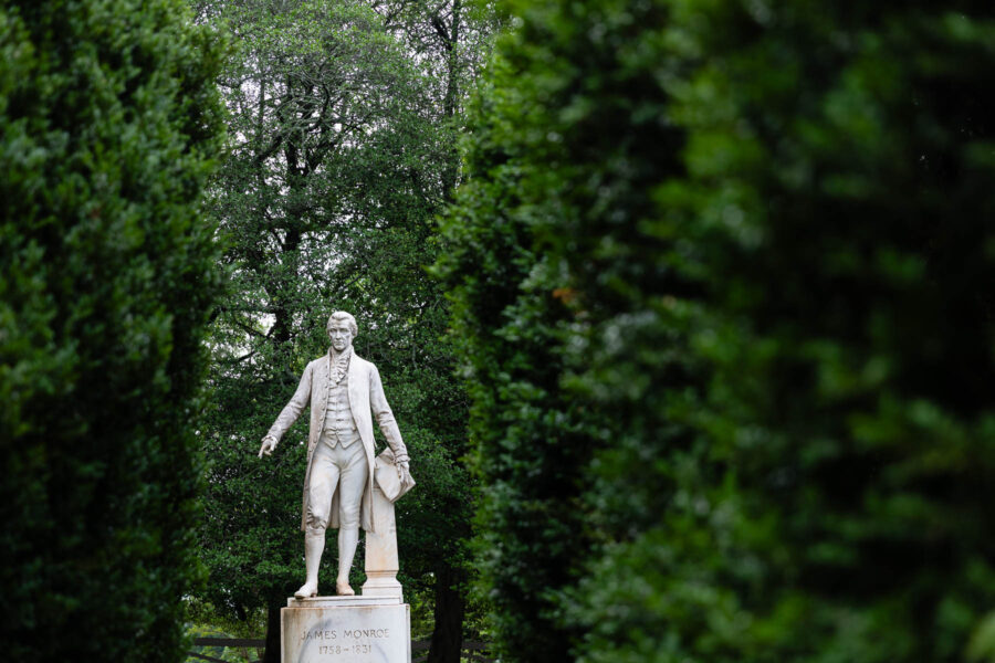 Stature of James Monroe with dense evergreen trees on either sides.