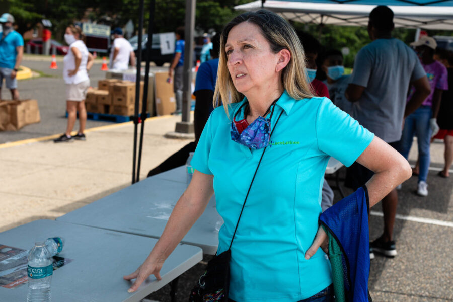 A woman in a bright blue ecoLatinos shirt leans against a table at an event.