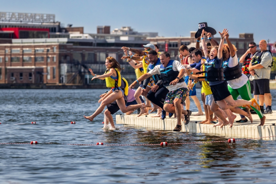 More than a dozen people jump into Baltimore’s Inner Harbor for a celebratory swim on a sunny day.