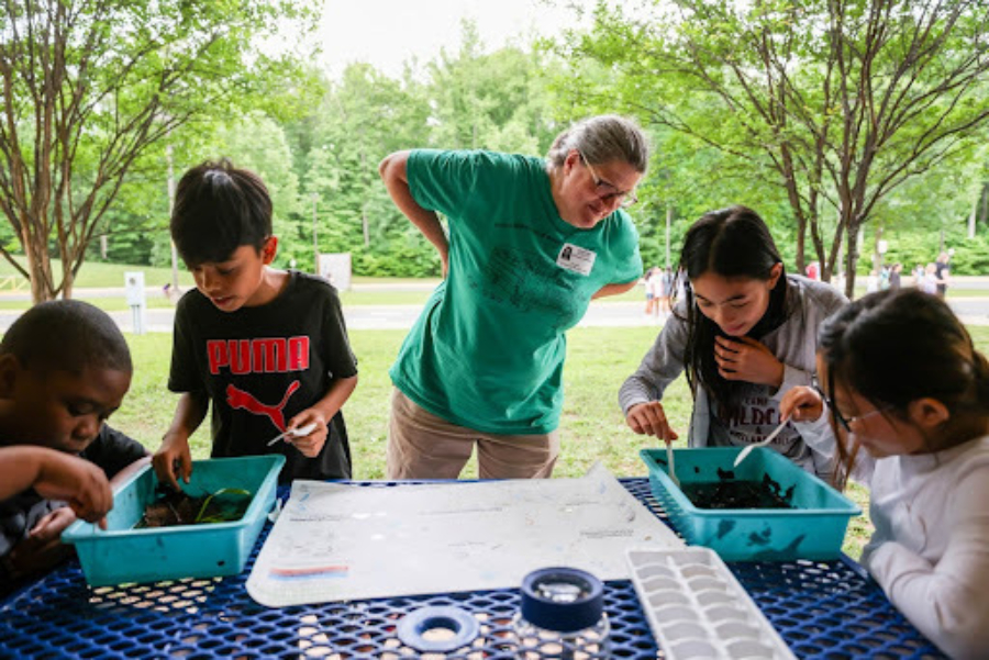 A teacher supervises engaged students completing a science project outside.