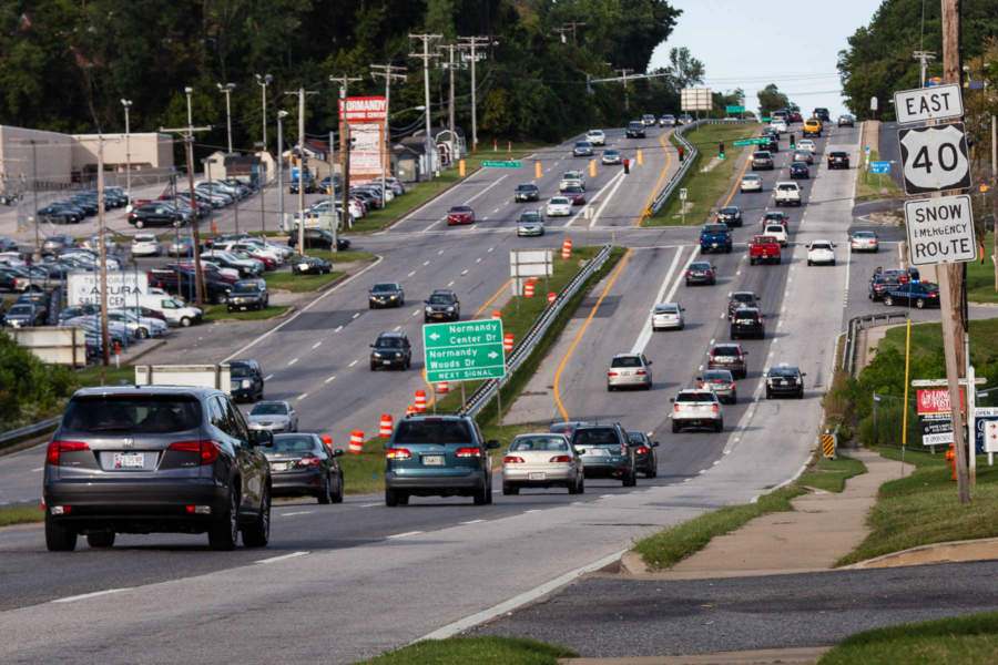 Cars drive along a suburban roadway that is home to car dealerships, shopping centers and other retailers.