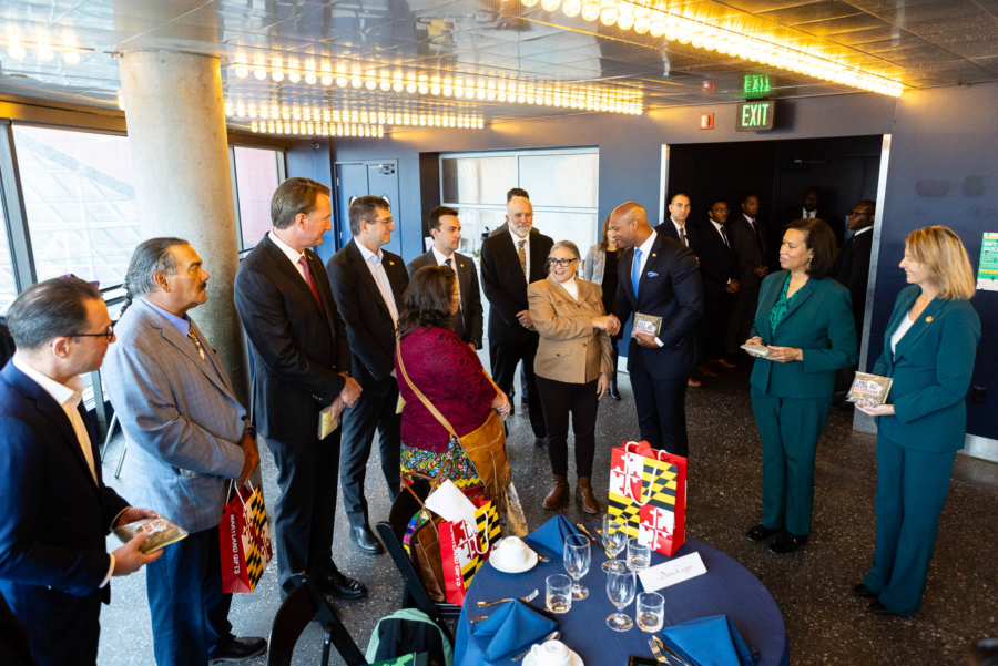 People in business professional clothing stand with four members of Native American tribes, holding gifts.