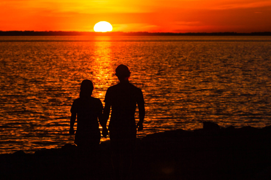 Silhouette of two people watching the sunset on the water.