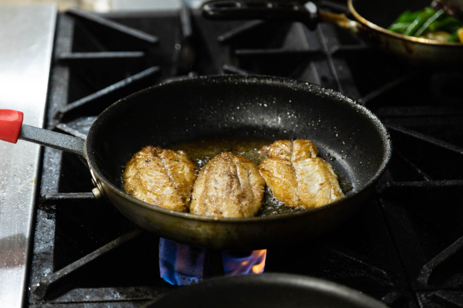 Fish fillets are cooked with oil in a frying pan.