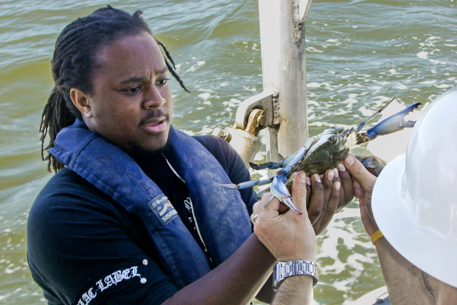 A youth conservation corps member carefully holds a blue crab while boating on the Chesapeake Bay