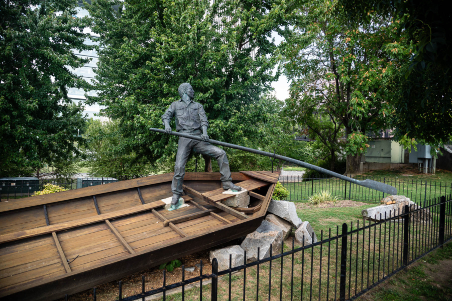 Sculpture depicting an African-American man in a small working boat, in a fenced in area of the park.