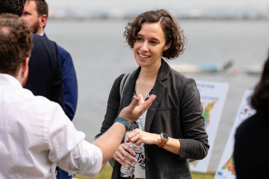 A woman in a suit jacket holds a water bottle while talking to a man in a dress shirt.