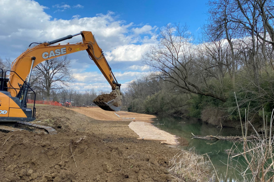 An excavator moves dirt near a stream restoration site.