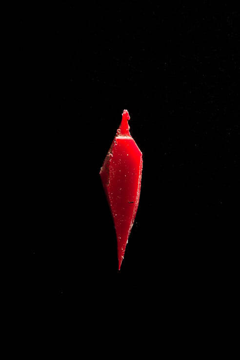 close up image on black background: a single jagged red piece of microplastic