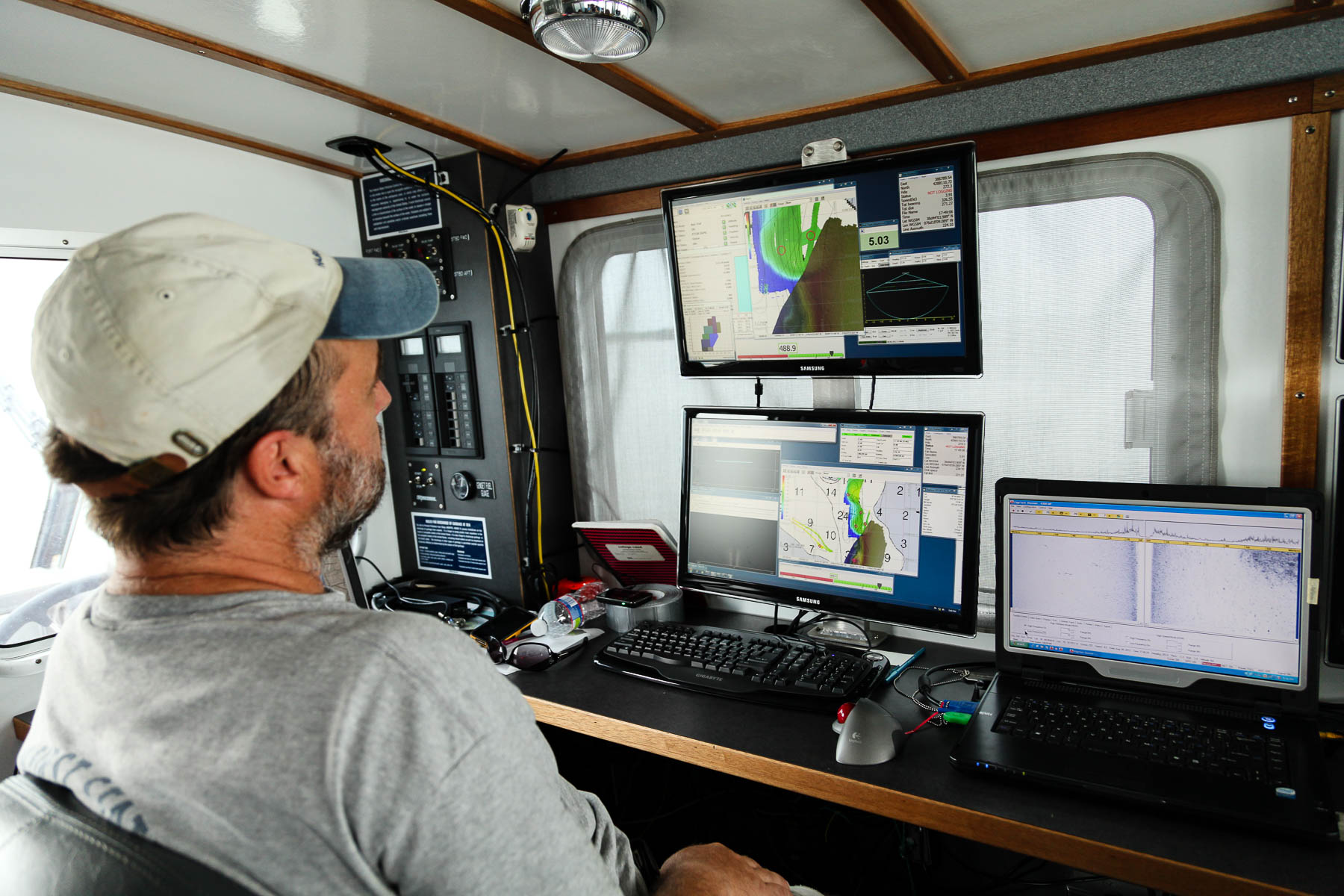 a man in the cabin of a boat looks at sonar maps on two computer screens