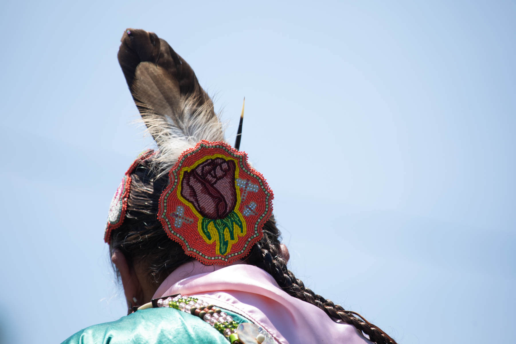 The back of a woman's head is shown with a beaded headpiece and feather