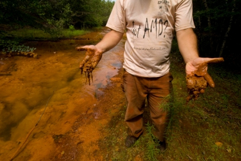 A person dips their hands into the Lackawanna River south of the borehole and shows how orange the mud is.
